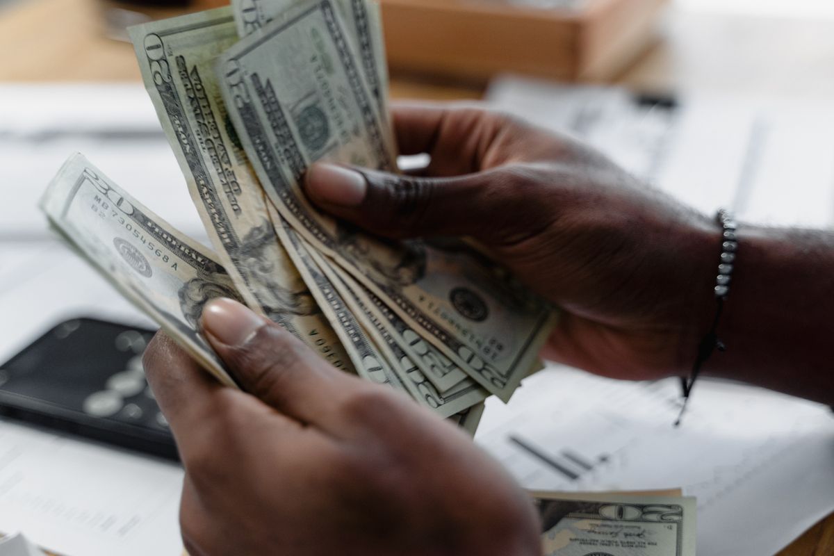 Hands counting US dollar banknotes over paperwork on a desk.