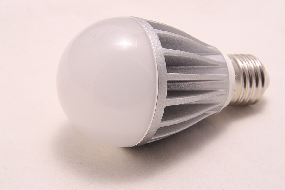 An unlit light bulb with a white dome, ribbed silver body and screw base lies on a pale surface.