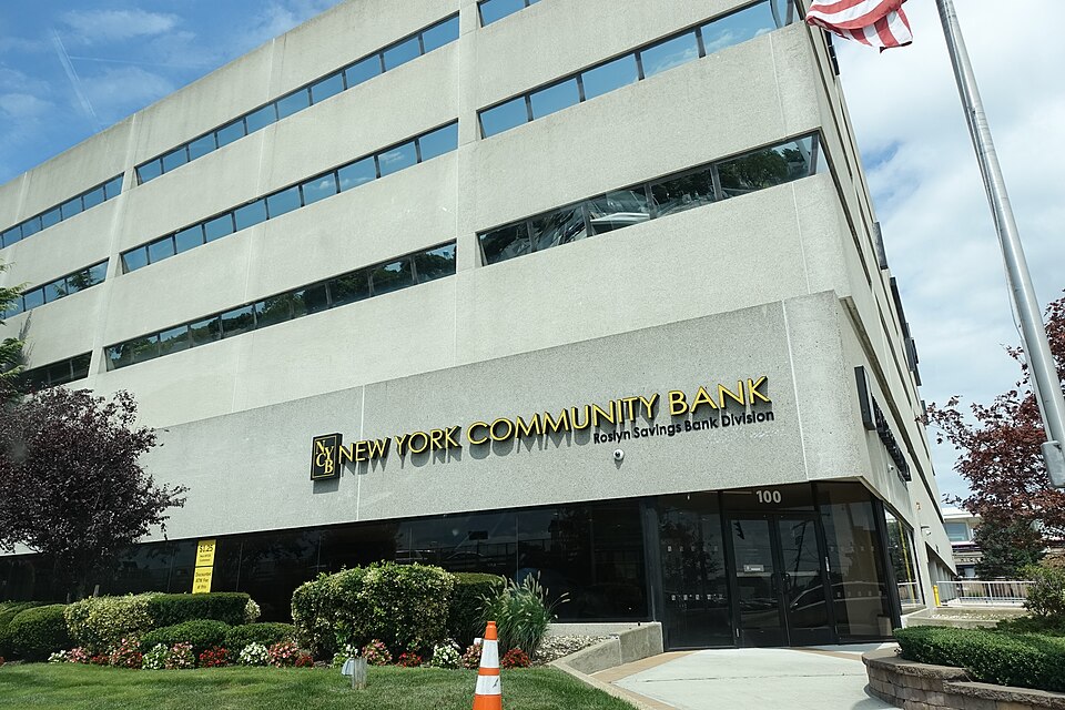 A multi-story building displays New York Community Bank and Roslyn Savings Bank Division signs above a landscaped entrance.