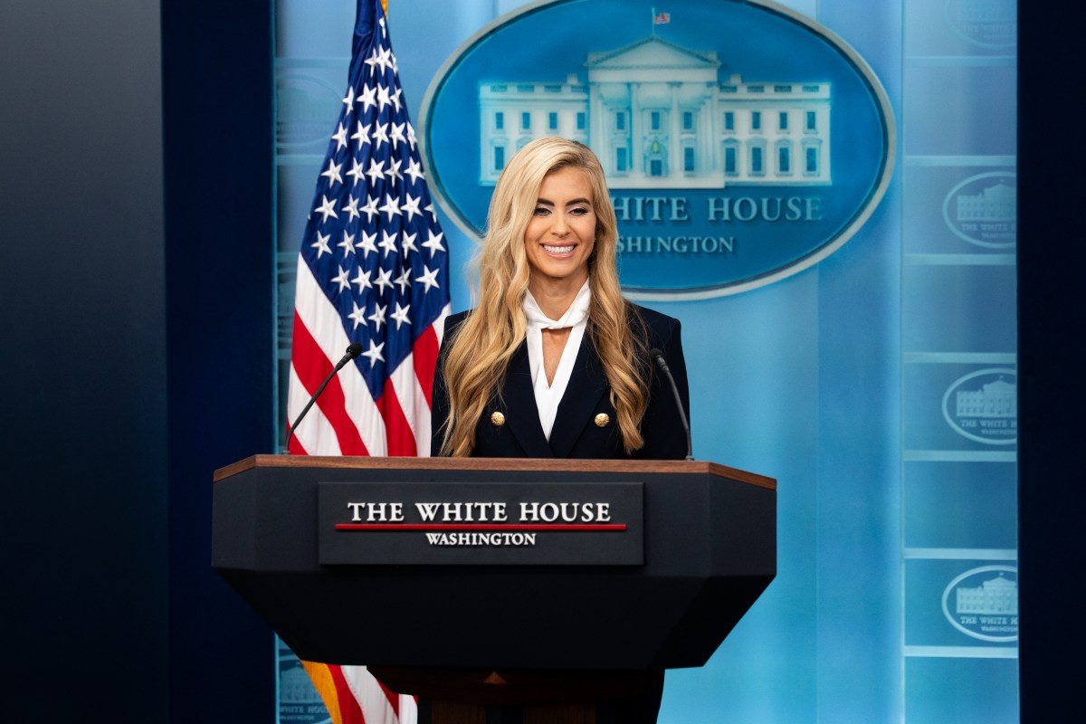 Katie Zacharia stands behind the White House briefing podium beside a U.S. flag.