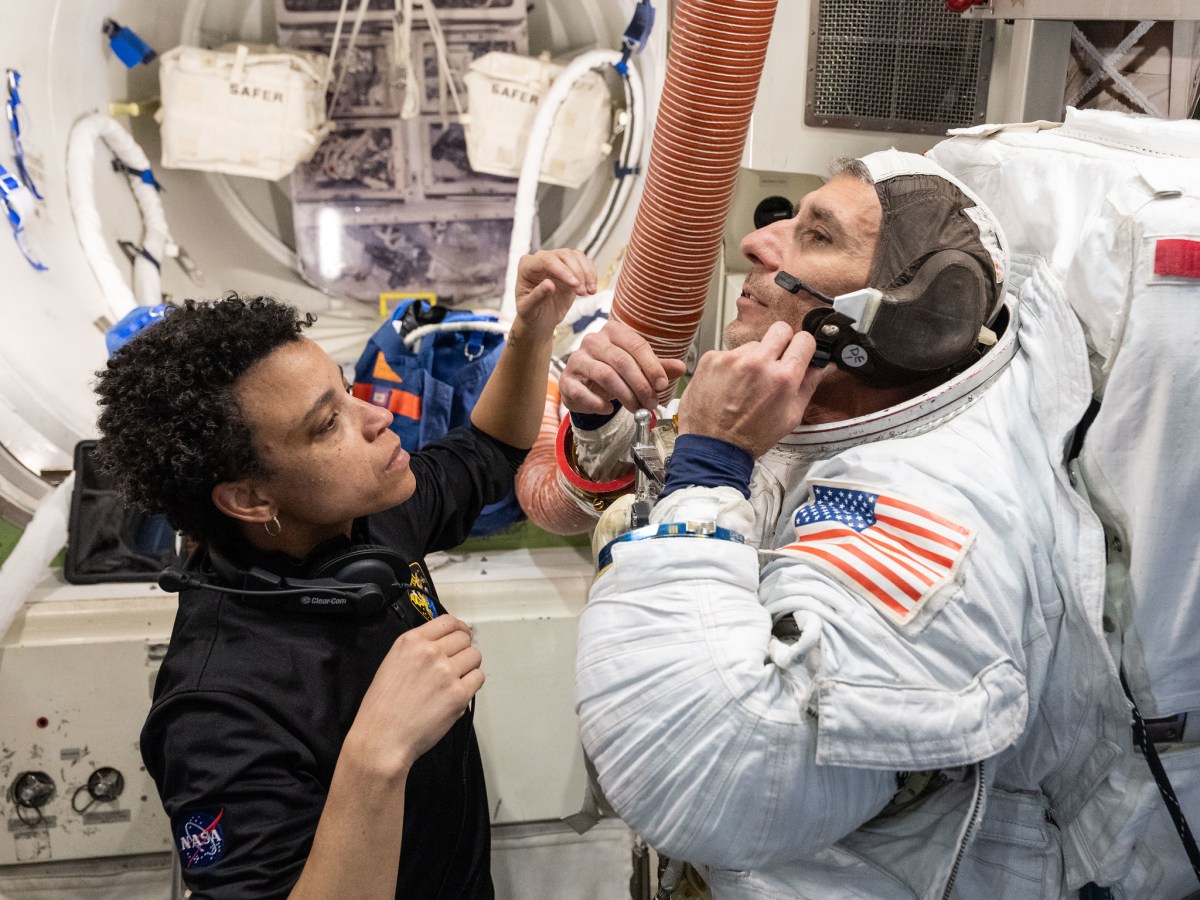 Jessica Watkins assists Luke Delaney, who is wearing a spacesuit, inside an airlock simulator during training.