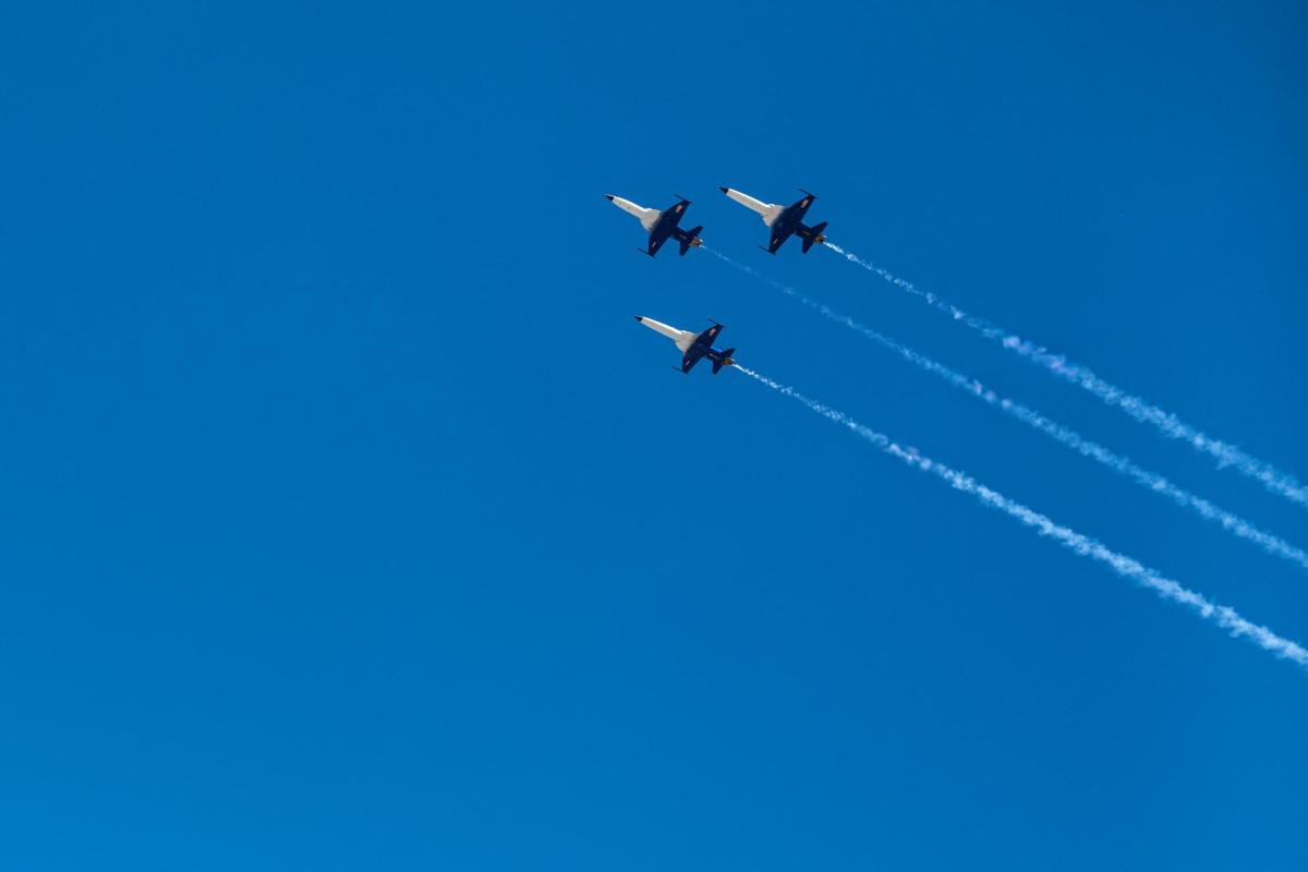 Three F-5 jets fly in formation against a blue sky, trailing white smoke.