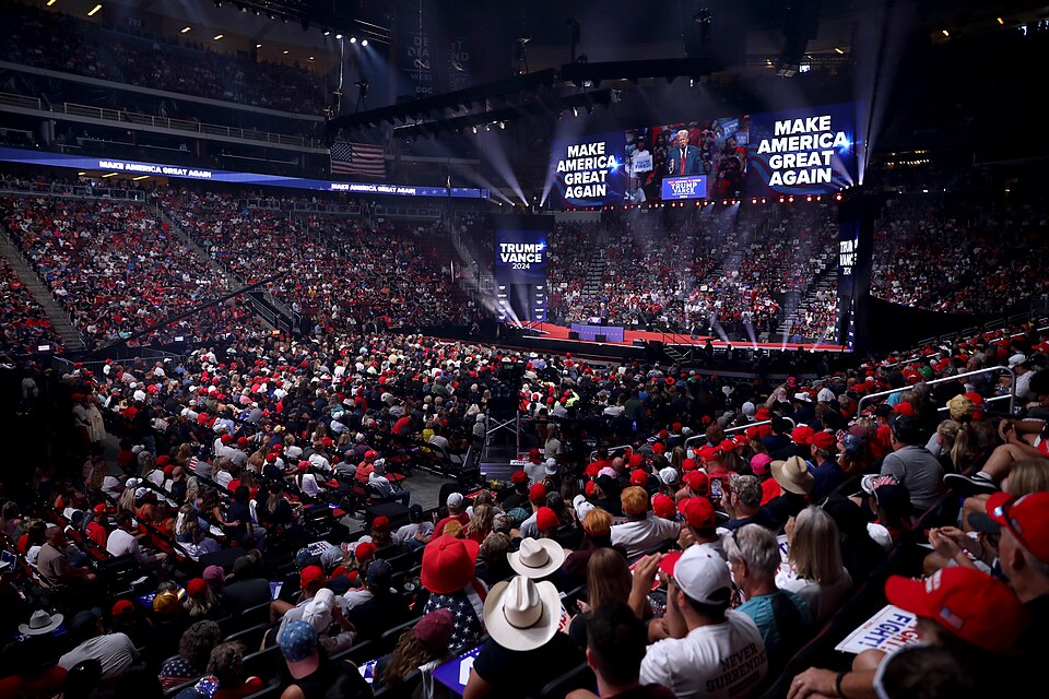 Archive photograph of a crowd at a Donald Trump campaign rally, with a stage and large screens in an arena.