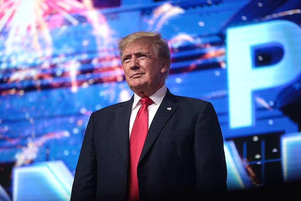 Archive photograph of Donald Trump in a dark suit and red tie against a blue stage backdrop.